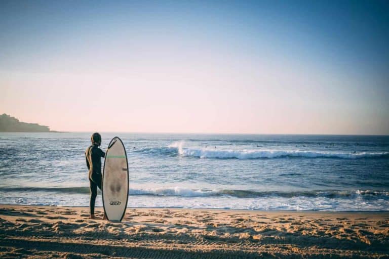Surfer steht mit Surfbrett am Strand